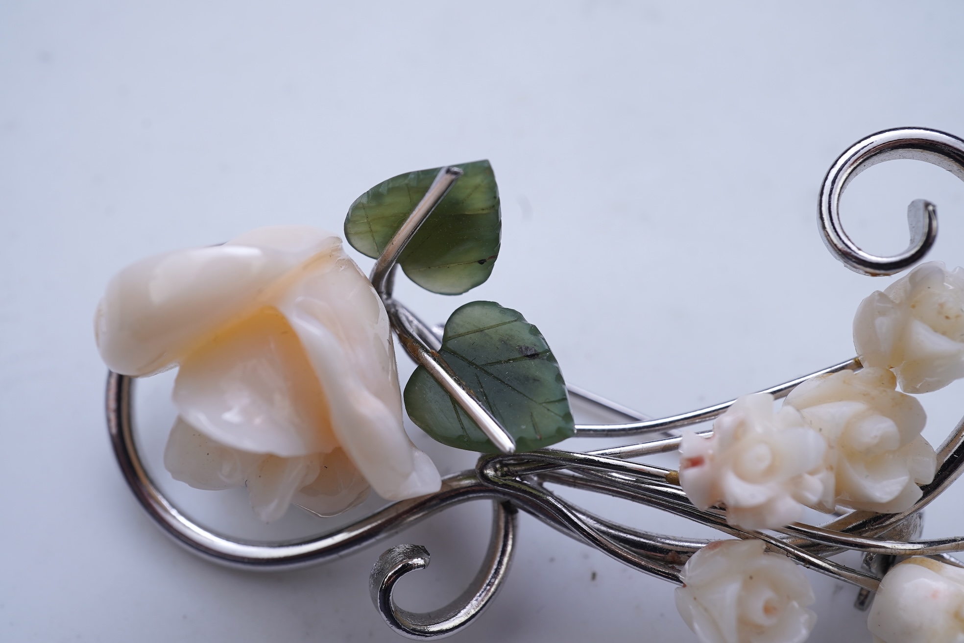 A white coral and nephrite brooch, designed as a spray of roses in carved white coral with nephrite leaves, on a scrolled white gold mount, length 5.5cm, stamped 14K, gross weight 11 grams